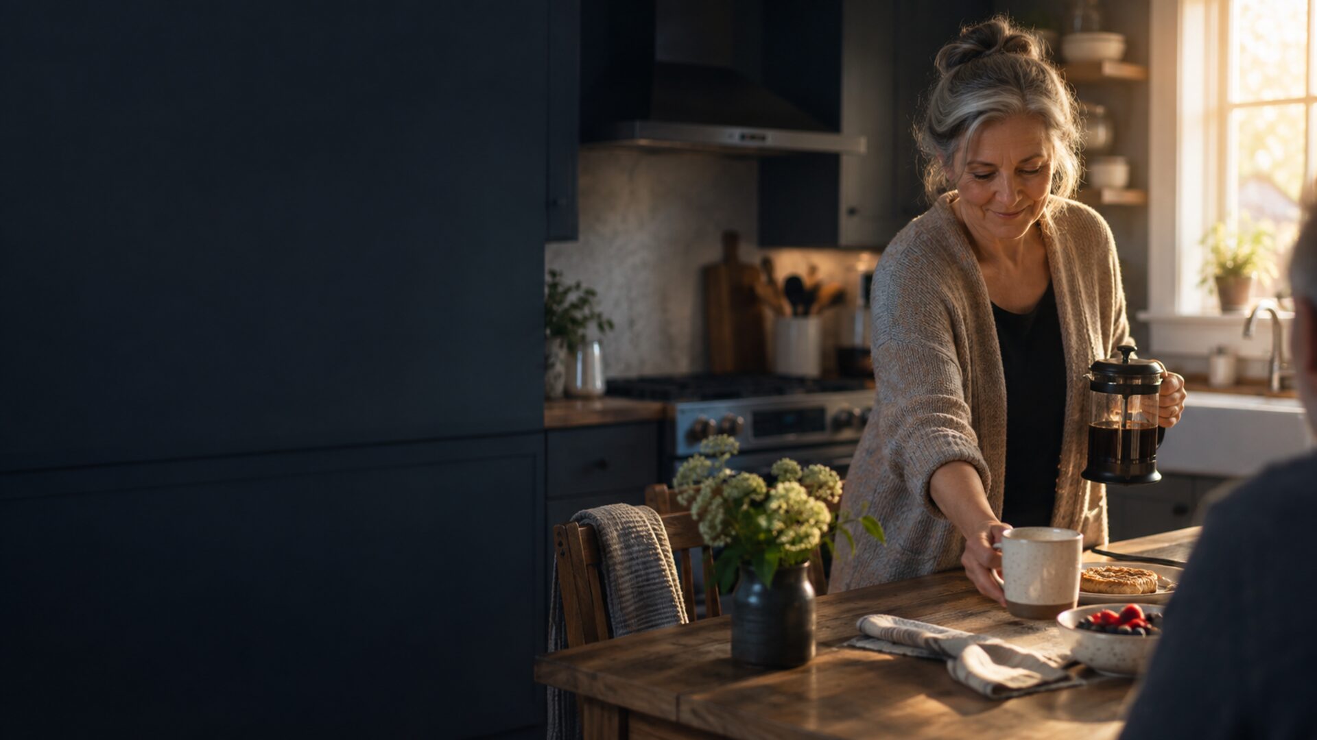 A woman offering coffee across a kitchen table in the morning